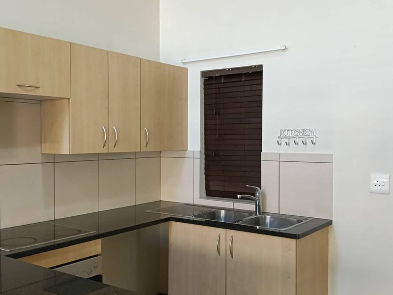 A functional kitchen featuring light wood laminate cabinetry, dark granite countertops, a stainless steel double sink, and a built-in electric hob.