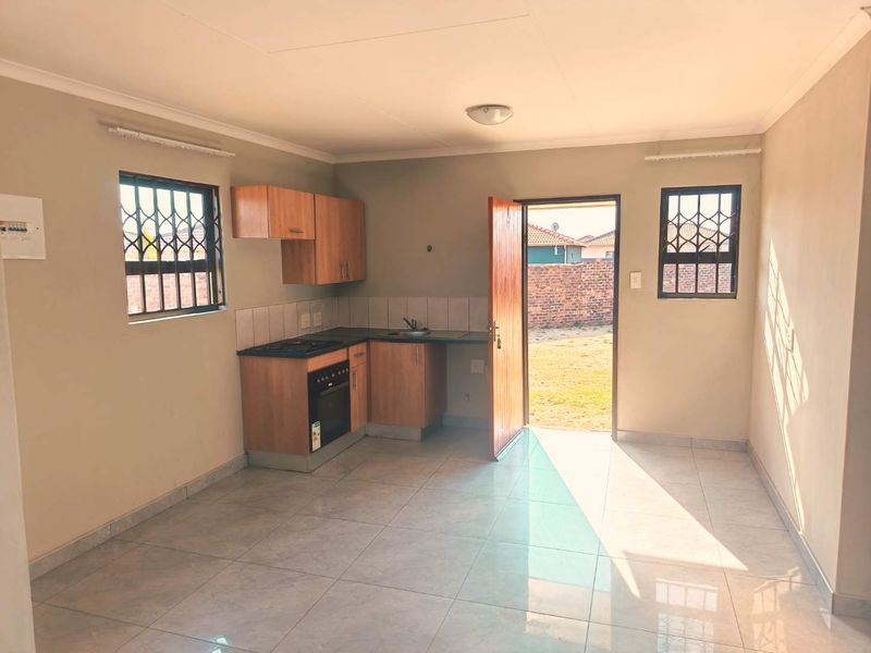 An open-plan kitchen area featuring built-in cabinetry, an oven, a hob, and tiled flooring, with direct access to the rear garden.