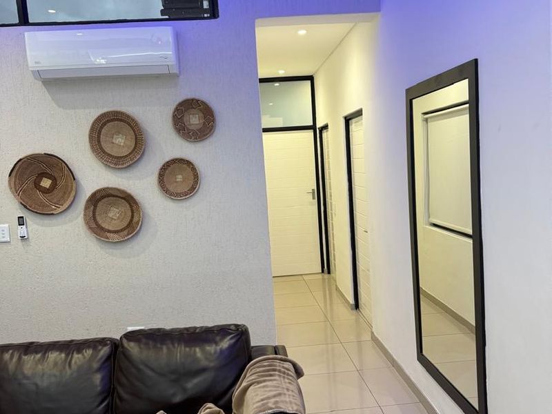 A modern living area featuring tiled flooring, recessed lighting, and a wall-mounted air conditioning unit, leading into a hallway with multiple internal doors.