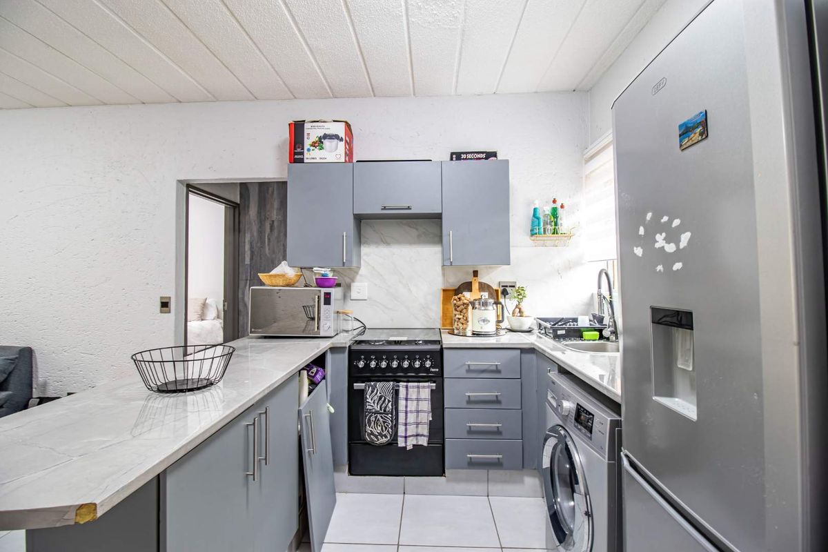 Compact kitchen featuring grey cabinetry, marble-effect countertops, integrated stove, and dedicated space for laundry appliances, offering a functional and modern layout.