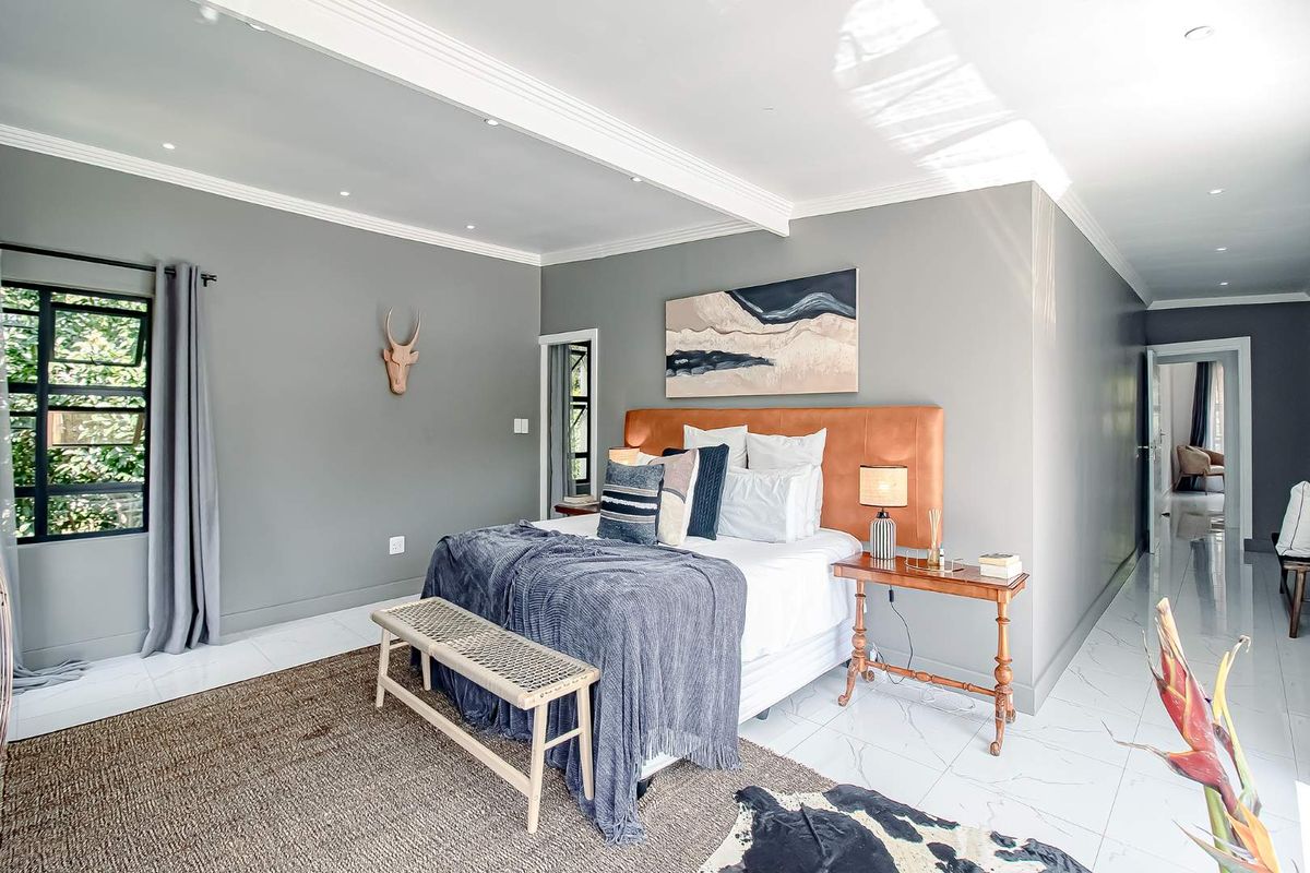 Spacious bedroom featuring neutral grey walls, crown molding, recessed lighting, and polished white tiled flooring with a view of the garden.