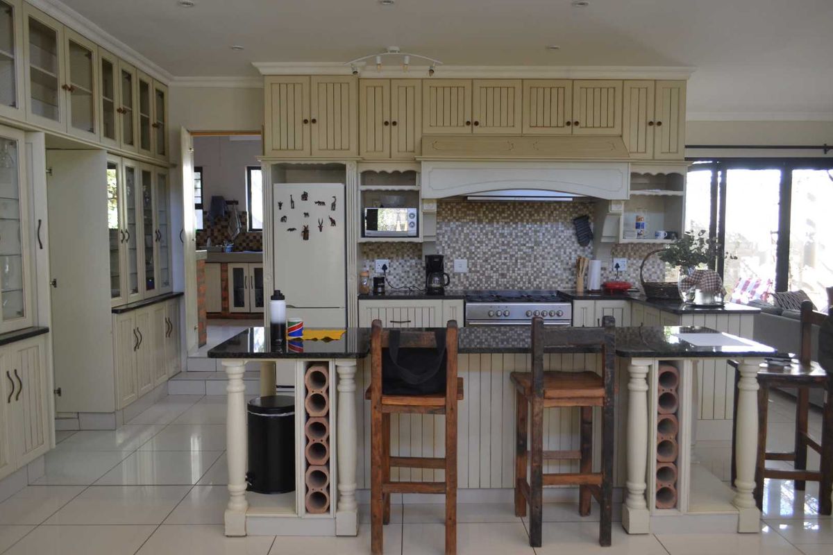 Spacious kitchen featuring cream-colored cabinetry, granite countertops, a central island with integrated wine storage, and a mosaic tile backsplash.
