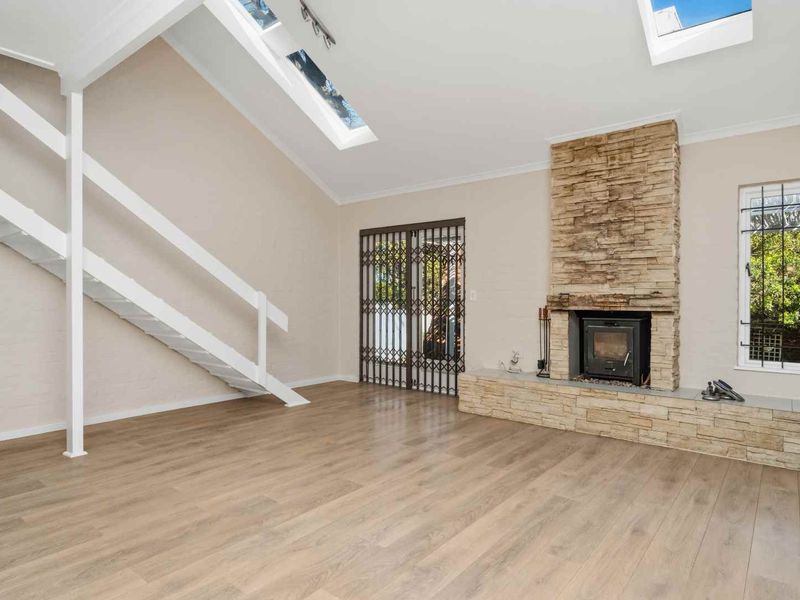 Spacious living room featuring a stone fireplace with a wood-burning stove, vaulted ceilings with skylights, and a staircase leading to an upper level.