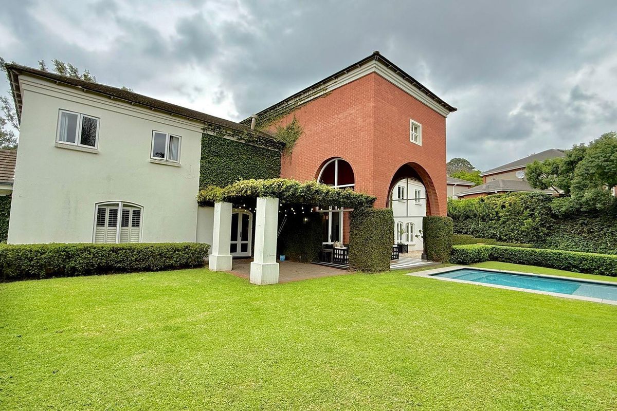 Rear view of the property featuring a manicured lawn, a swimming pool, and a covered patio area with architectural brick detailing.