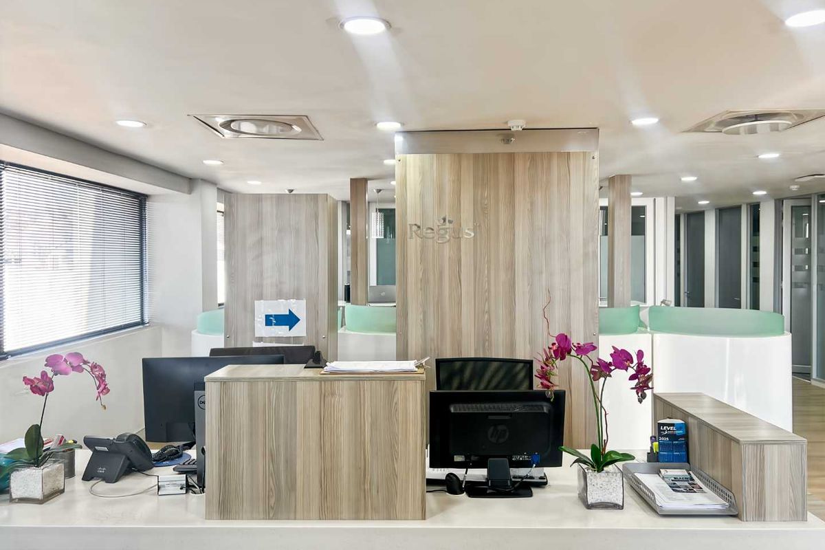 A professional office reception area featuring a modern wood-finish desk, recessed lighting, and glass partitions, creating a clean and welcoming corporate environment.