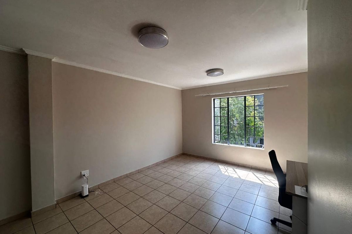 A bright, empty bedroom featuring neutral wall tones, tiled flooring, and a large window providing natural light and a view of greenery.