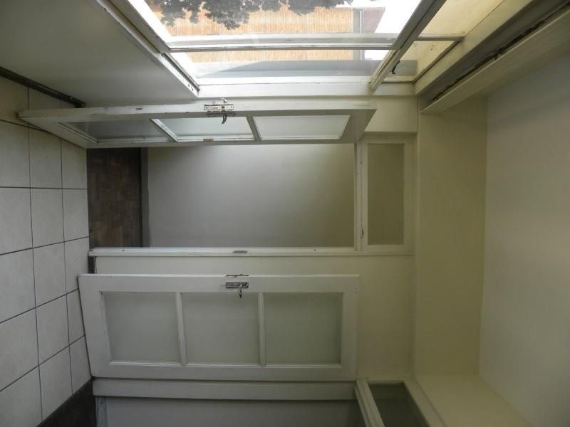 A small, enclosed balcony or sunroom area featuring tiled flooring, a skylight, and glass-paneled doors, currently in need of cosmetic refurbishment.