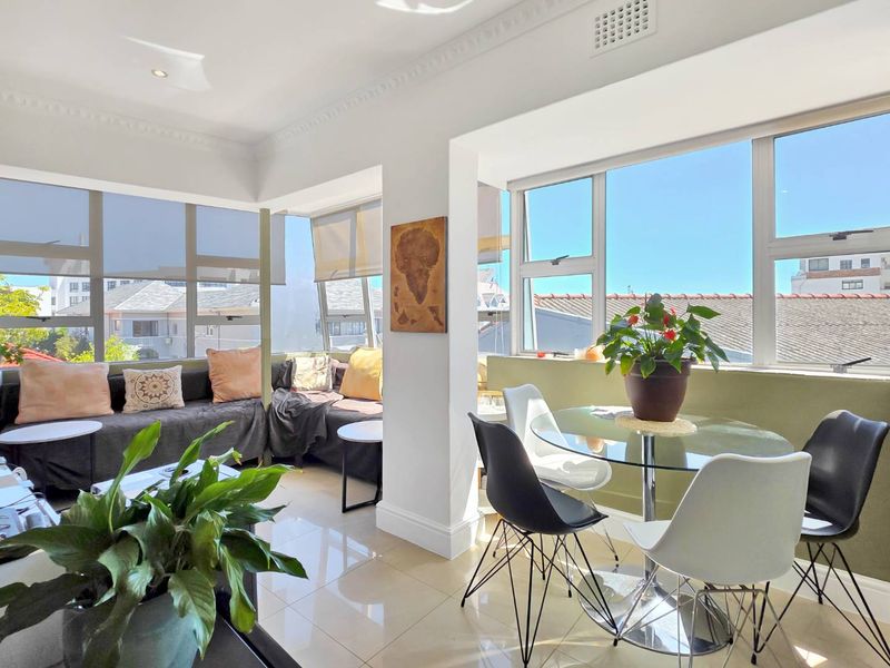Bright open-plan living and dining area featuring large windows, tiled flooring, and decorative ceiling cornices, offering ample natural light.