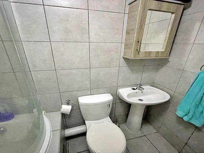 Compact bathroom featuring a pedestal basin, toilet, shower enclosure, and wall-mounted medicine cabinet with neutral tiled finishes.