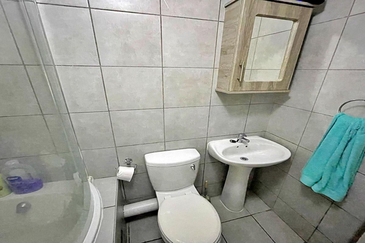 Compact bathroom featuring a pedestal basin, toilet, shower enclosure, and wall-mounted medicine cabinet with neutral tiled finishes.