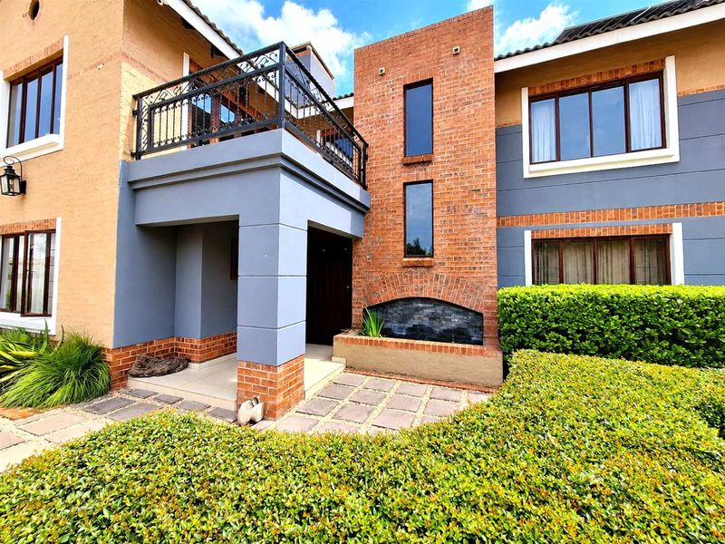 A well-maintained front exterior featuring a brick facade, a private balcony with wrought iron railings, and a landscaped garden with a built-in water feature.