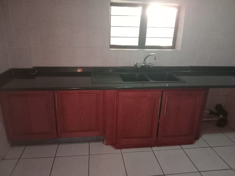 A functional kitchen area featuring dark granite countertops, wooden cabinetry, a double basin sink, and tiled finishes throughout.