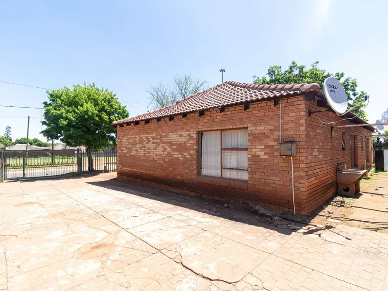 Rear view of a face brick house featuring a tiled roof, paved yard area, and perimeter metal fencing.