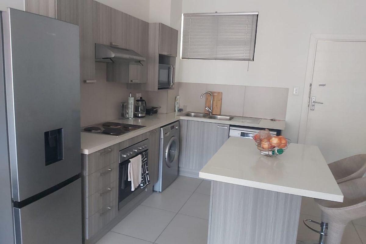 Modern kitchen featuring light wood-grain cabinetry, stone countertops, integrated stainless steel appliances, and a functional breakfast island with tiled flooring.