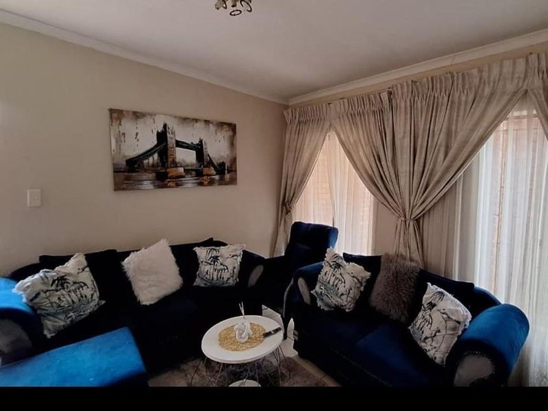 A comfortable living room featuring neutral wall tones, coving, and large windows dressed with floor-to-ceiling curtains.