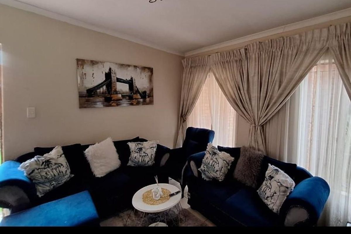 A comfortable living room featuring neutral wall tones, coving, and large windows dressed with floor-to-ceiling curtains.