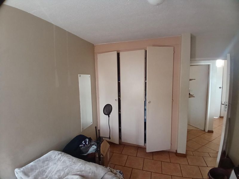 A bedroom featuring tiled flooring and a built-in wardrobe with white doors, offering functional storage space within the apartment.