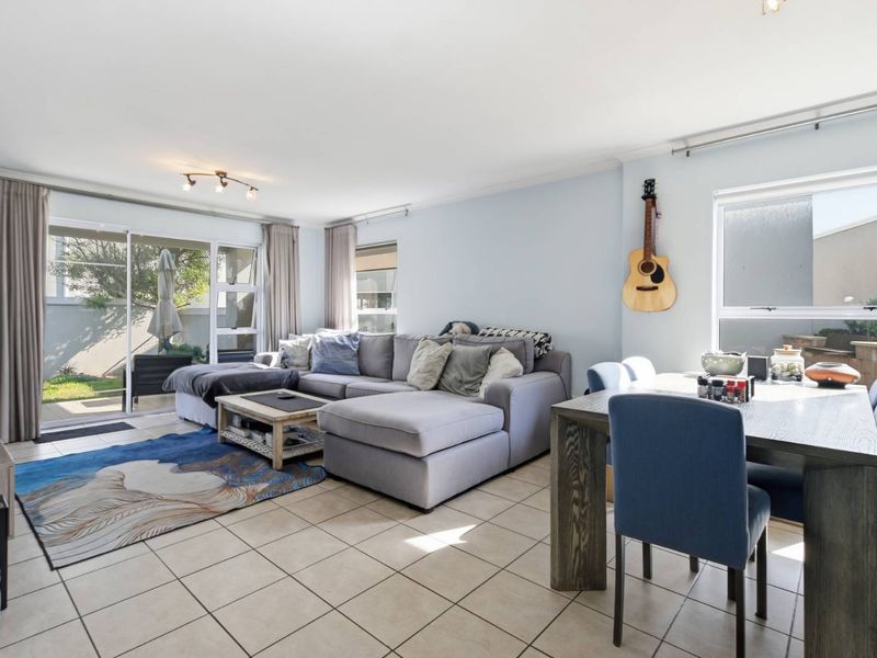 Bright open-plan living and dining area featuring tiled flooring and large sliding glass doors providing direct access to the outdoor patio and garden.