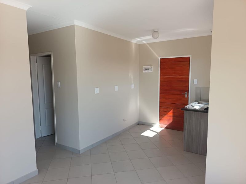 An open-plan living area featuring neutral wall tones, tiled flooring, and a small kitchenette counter, providing a clean and versatile space.
