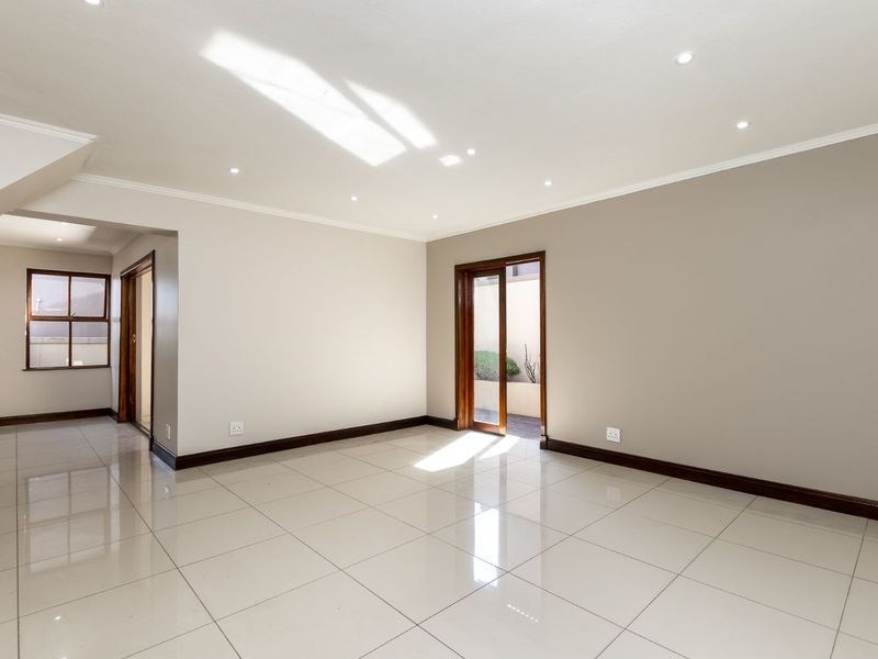 A bright, empty living area featuring polished porcelain tiles, recessed downlighting, and direct access to an outdoor space through a sliding glass door.