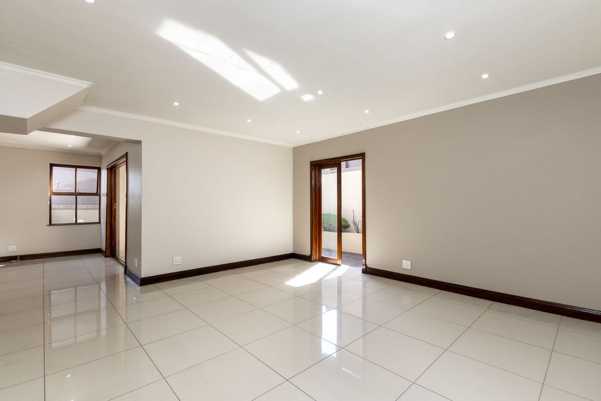 A bright, empty living area featuring polished porcelain tiles, recessed downlighting, and direct access to an outdoor space through a sliding glass door.