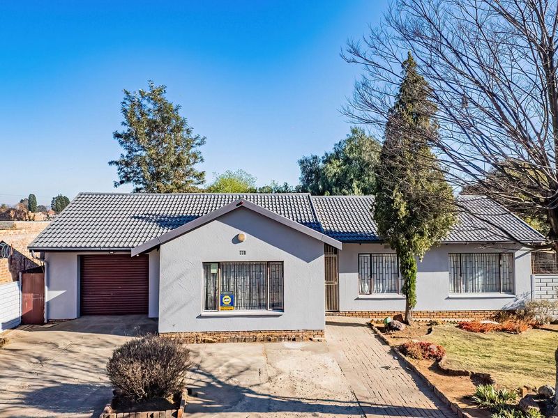 Front elevation of a single-story house featuring a tiled roof, integrated garage, security bars on windows, and a paved driveway with a front garden.