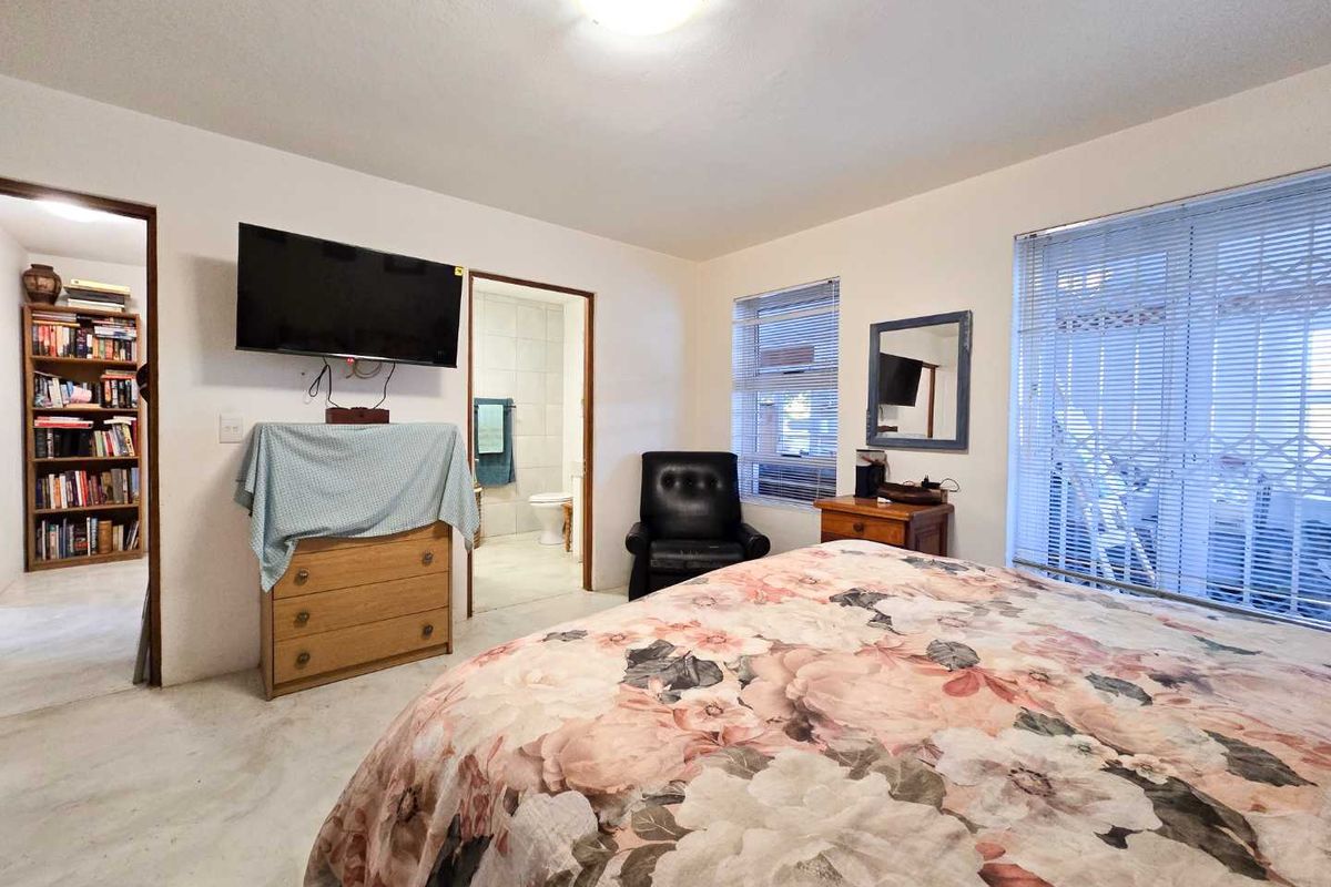A functional bedroom featuring an en-suite bathroom, large windows with venetian blinds, and security gates, providing a practical and well-lit living space.