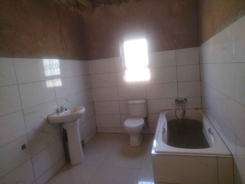 A bathroom in need of completion, featuring a pedestal basin, toilet, and bathtub with partially tiled walls and unfinished plasterwork.
