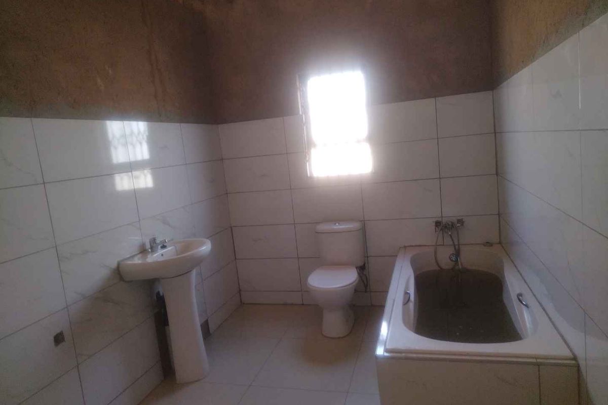 A bathroom in need of completion, featuring a pedestal basin, toilet, and bathtub with partially tiled walls and unfinished plasterwork.