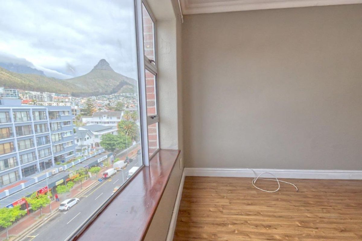 An empty bedroom featuring laminate flooring, coving, and a timber window sill with expansive views of the surrounding urban landscape and mountain.
