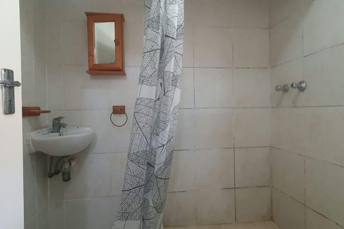 A compact bathroom featuring tiled walls, a wall-mounted basin, and a shower area, requiring cosmetic updates to improve its overall condition.