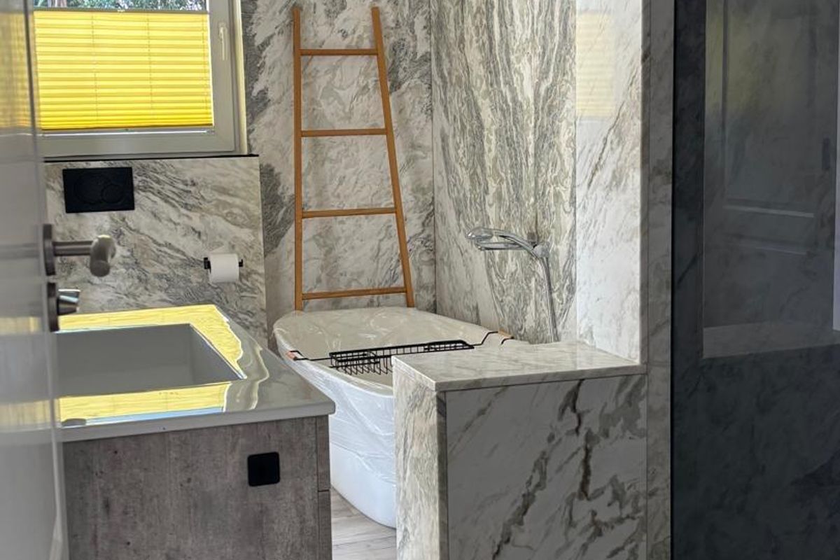 Modern bathroom featuring marble-clad walls, a built-in bathtub, a glass-enclosed shower, and a contemporary vanity unit with integrated sink.
