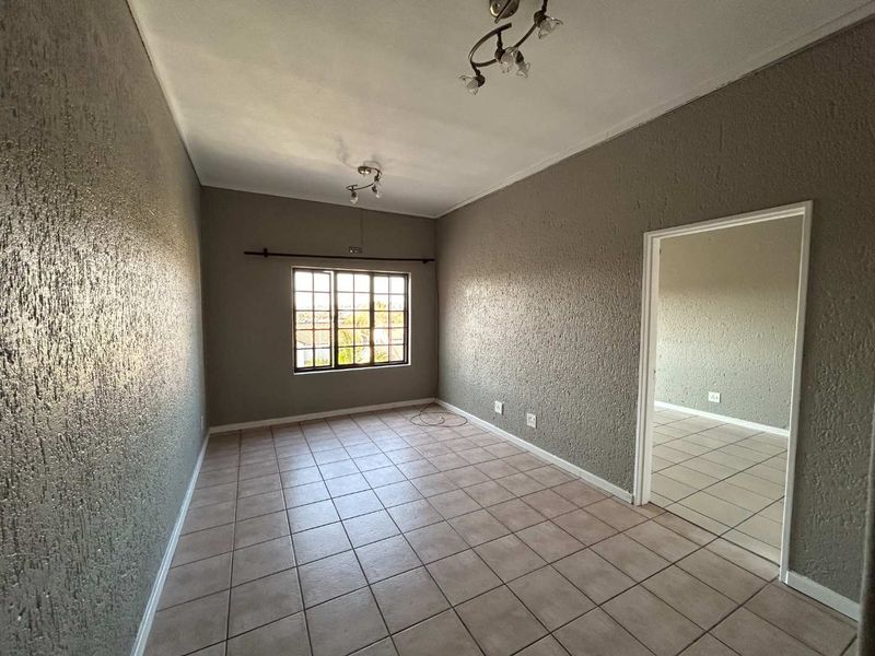 An empty living room featuring neutral textured walls, tiled flooring, and natural light from a window, offering a blank canvas for interior design.