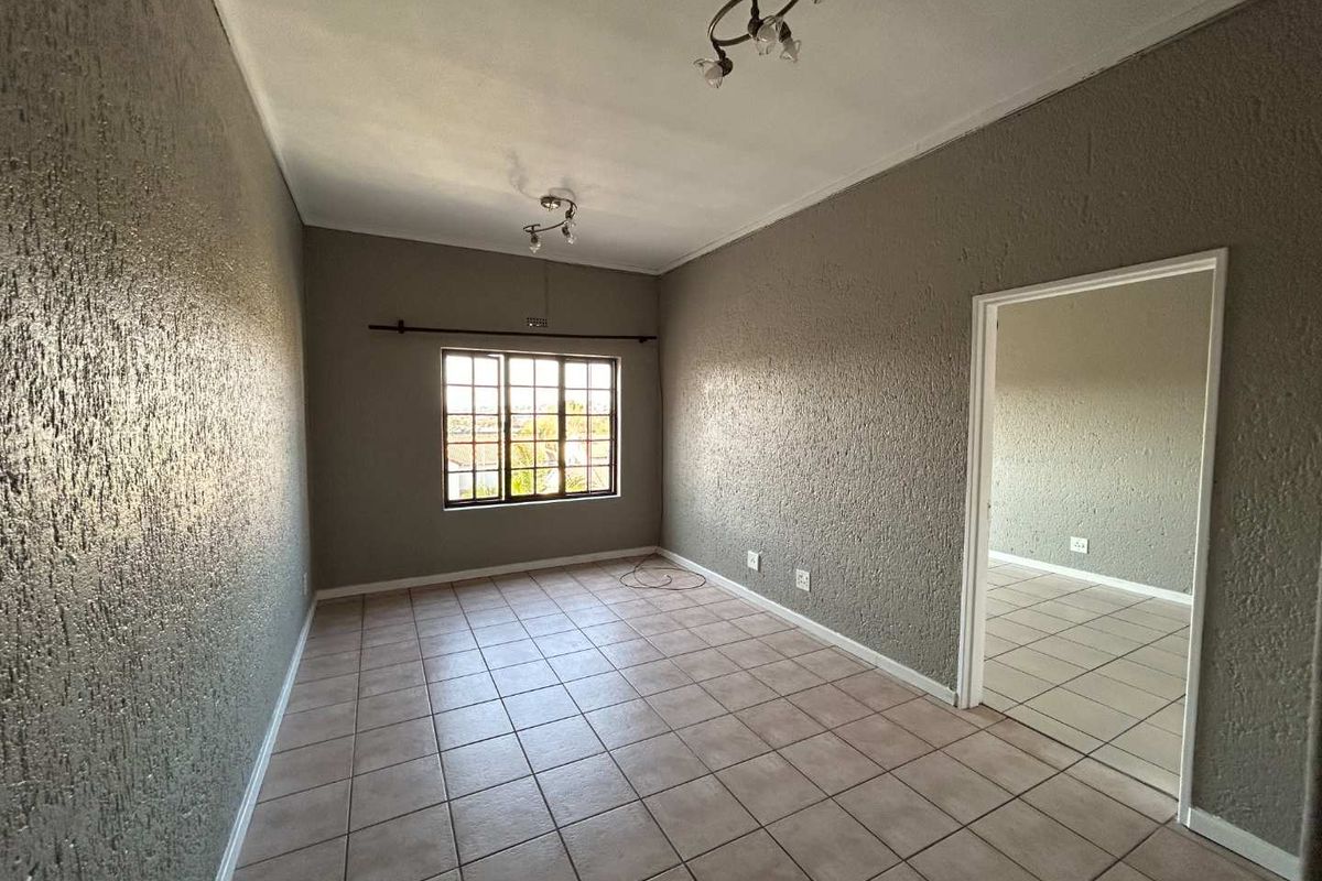 An empty living room featuring neutral textured walls, tiled flooring, and natural light from a window, offering a blank canvas for interior design.