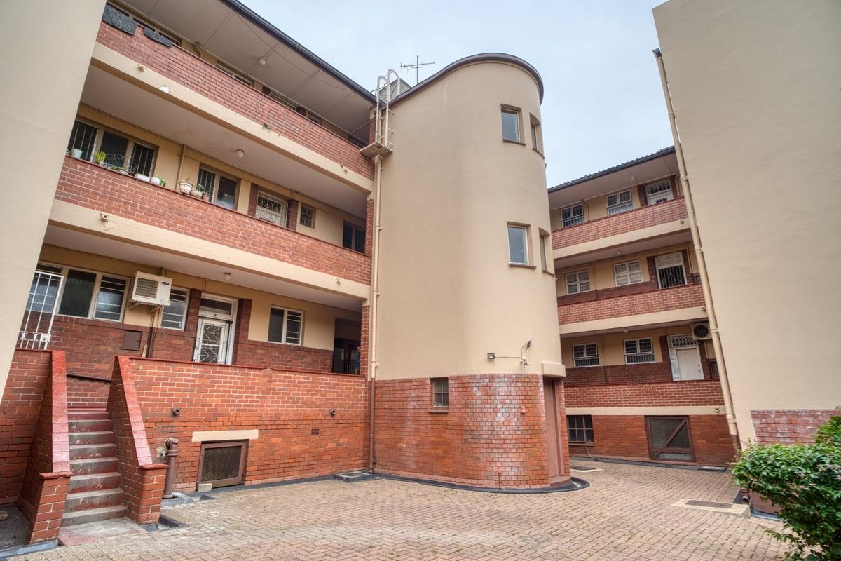 A view of the apartment complex rear courtyard featuring multi-level brick balconies, a central curved architectural feature, and paved ground area.