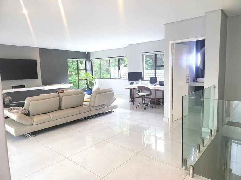 Spacious open-plan living area featuring polished porcelain floor tiles, a modern glass balustrade, and a contemporary feature wall with integrated television space.