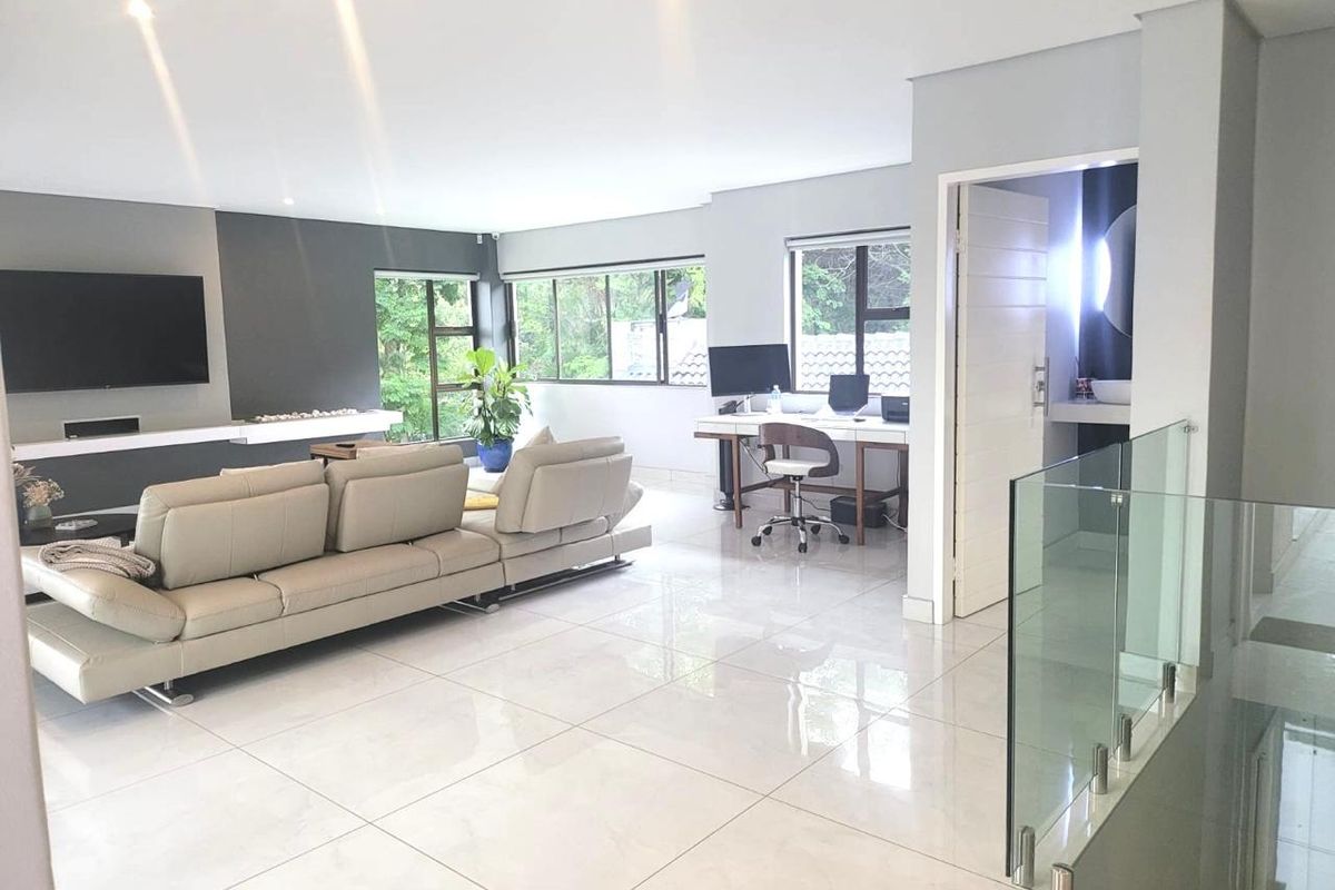 Spacious open-plan living area featuring polished porcelain floor tiles, a modern glass balustrade, and a contemporary feature wall with integrated television space.