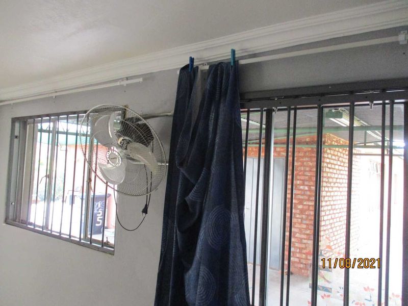 A covered patio area featuring security bars on windows and doors, showing signs of wear on the wall finishes.