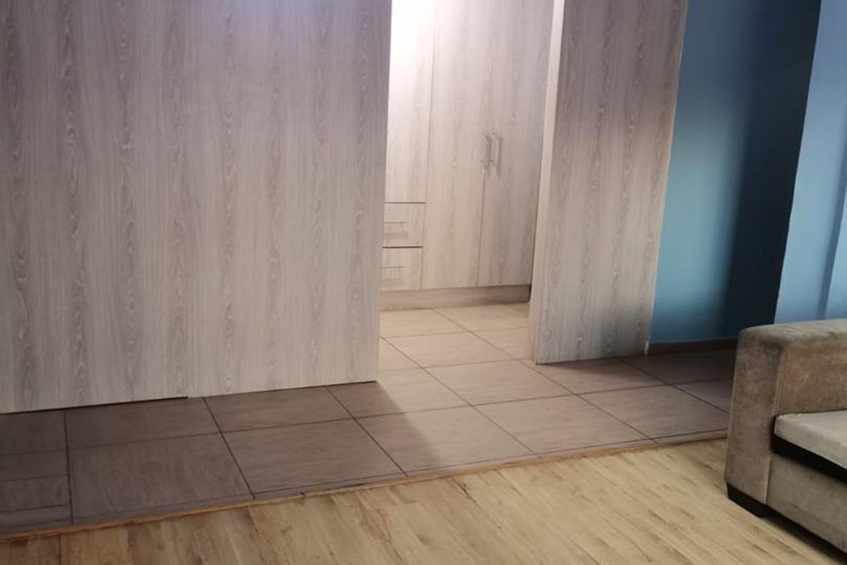 A bedroom interior featuring built-in wooden cabinetry, tiled flooring in the wardrobe area, and laminate wood flooring in the main living space.