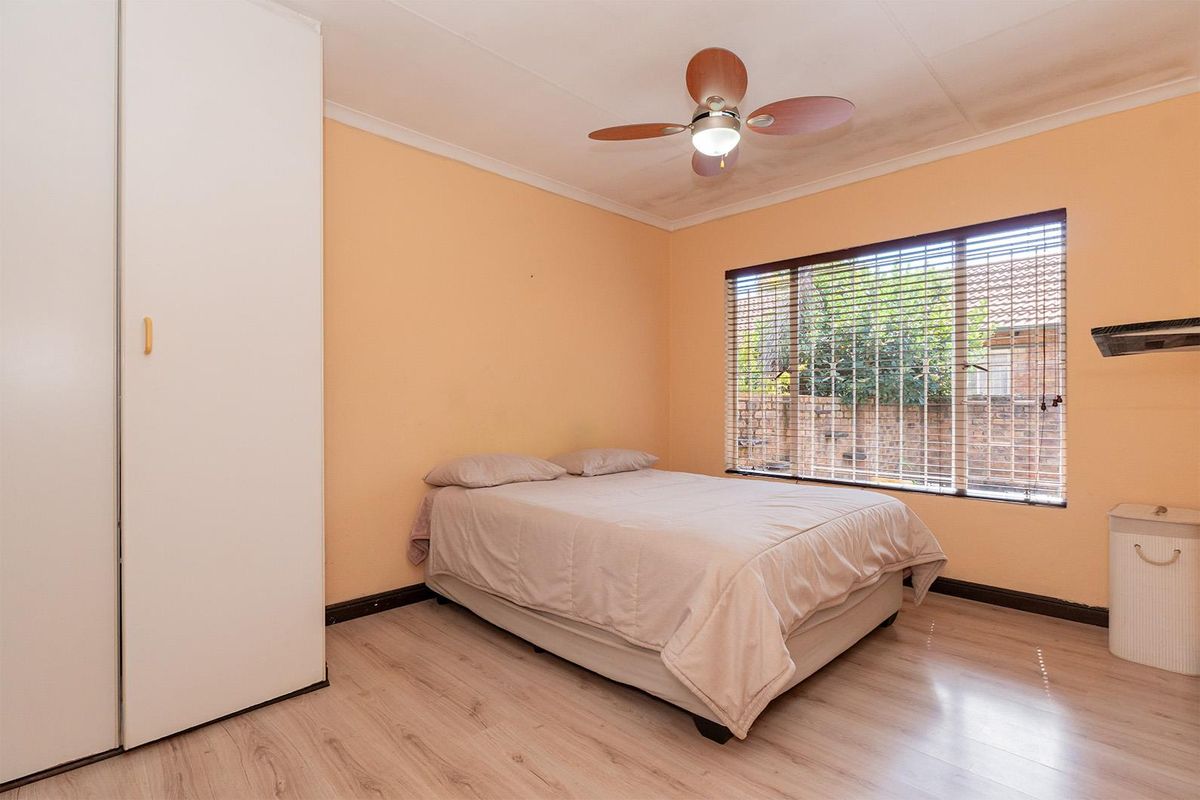 A bedroom featuring light wood-look flooring, built-in wardrobe, and a ceiling fan, with natural light provided by a large window.