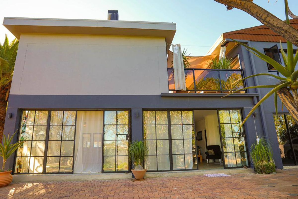 Rear elevation featuring large steel-framed glass doors opening onto a paved patio, with an upper-level balcony and glass balustrade.