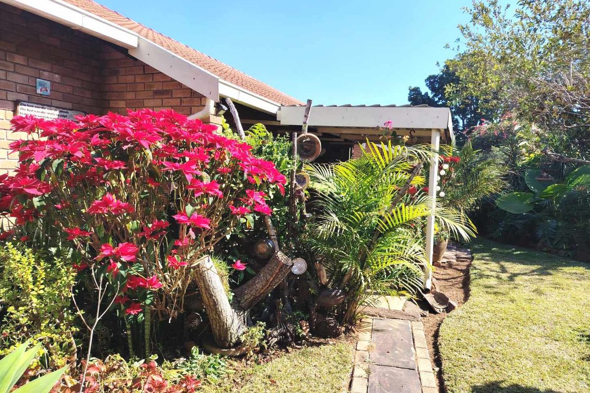 A view of the rear exterior featuring a brick facade, a covered patio area, and a well-established garden with a paved walkway.