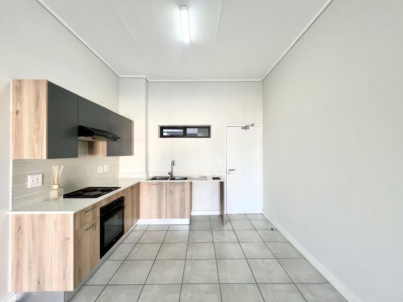 A clean, modern kitchen featuring light wood-tone cabinetry, dark grey upper cabinets, integrated appliances, and neutral tiled flooring in an open-plan layout.