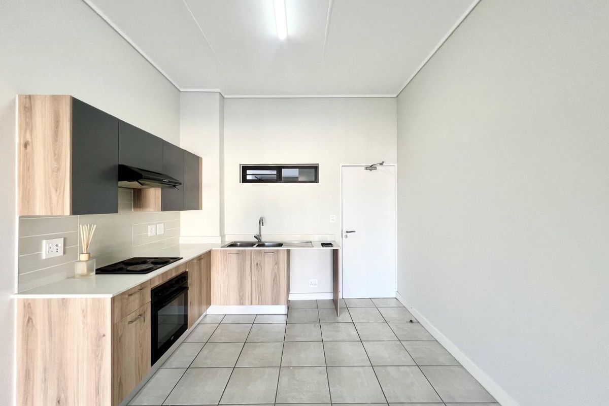 A clean, modern kitchen featuring light wood-tone cabinetry, dark grey upper cabinets, integrated appliances, and neutral tiled flooring in an open-plan layout.
