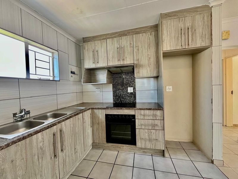 A functional kitchen featuring wood-look cabinetry, a built-in oven and hob, tiled splashbacks, and a double sink with ample storage space.