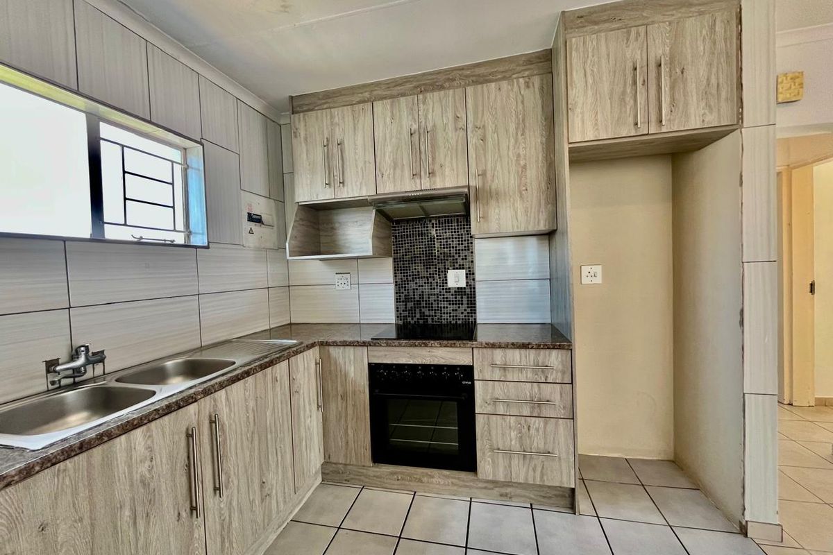 A functional kitchen featuring wood-look cabinetry, a built-in oven and hob, tiled splashbacks, and a double sink with ample storage space.