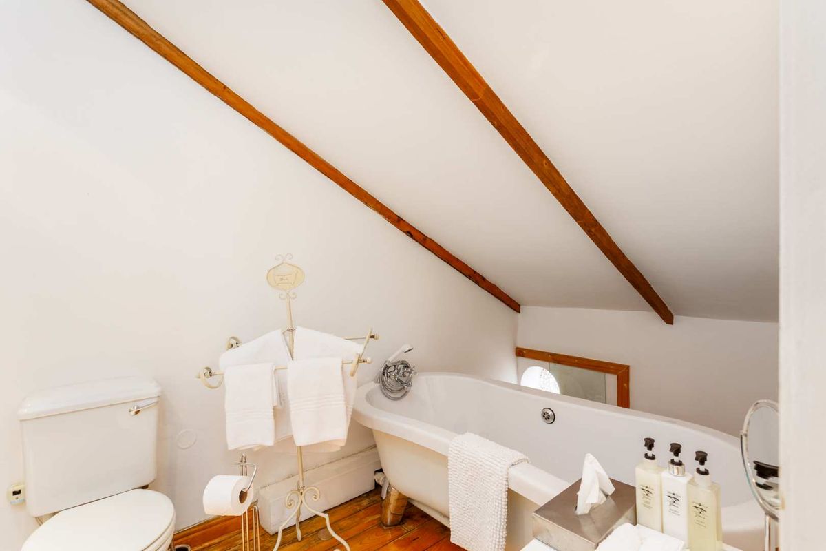 A charming attic-style bathroom featuring a classic clawfoot bathtub, exposed timber ceiling beams, and warm hardwood flooring.