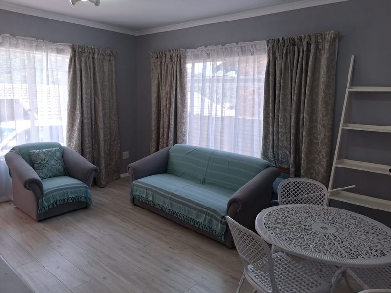 A well-maintained living room featuring light-toned laminate flooring and neutral grey walls, providing a clean and functional space.