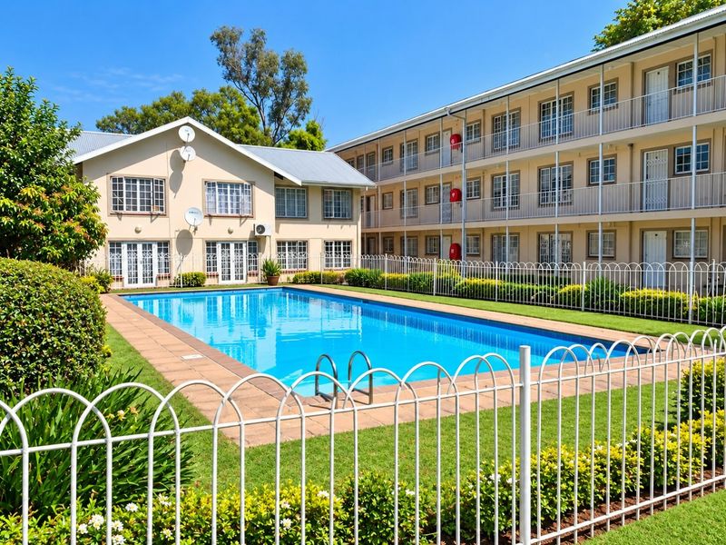 A well-maintained communal swimming pool area featuring a clear blue pool, metal safety fencing, and views of the surrounding apartment complex.