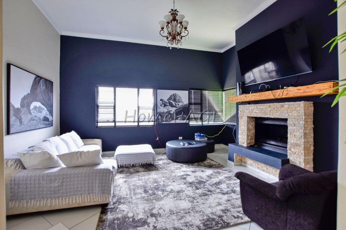 Spacious living room featuring a stone-clad fireplace with a timber mantel, dark accent walls, and tiled flooring.